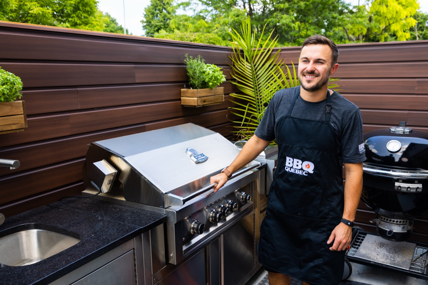 Un pitmaster BBQ Québec souriant dans une cuisine extérieure résidentielle